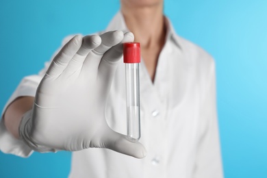 Female doctor holding empty test tube on color background, closeup. Medical object