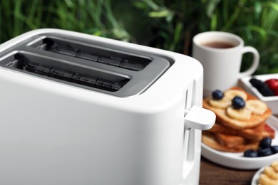 Photo of Toaster and breakfast on wooden table, closeup