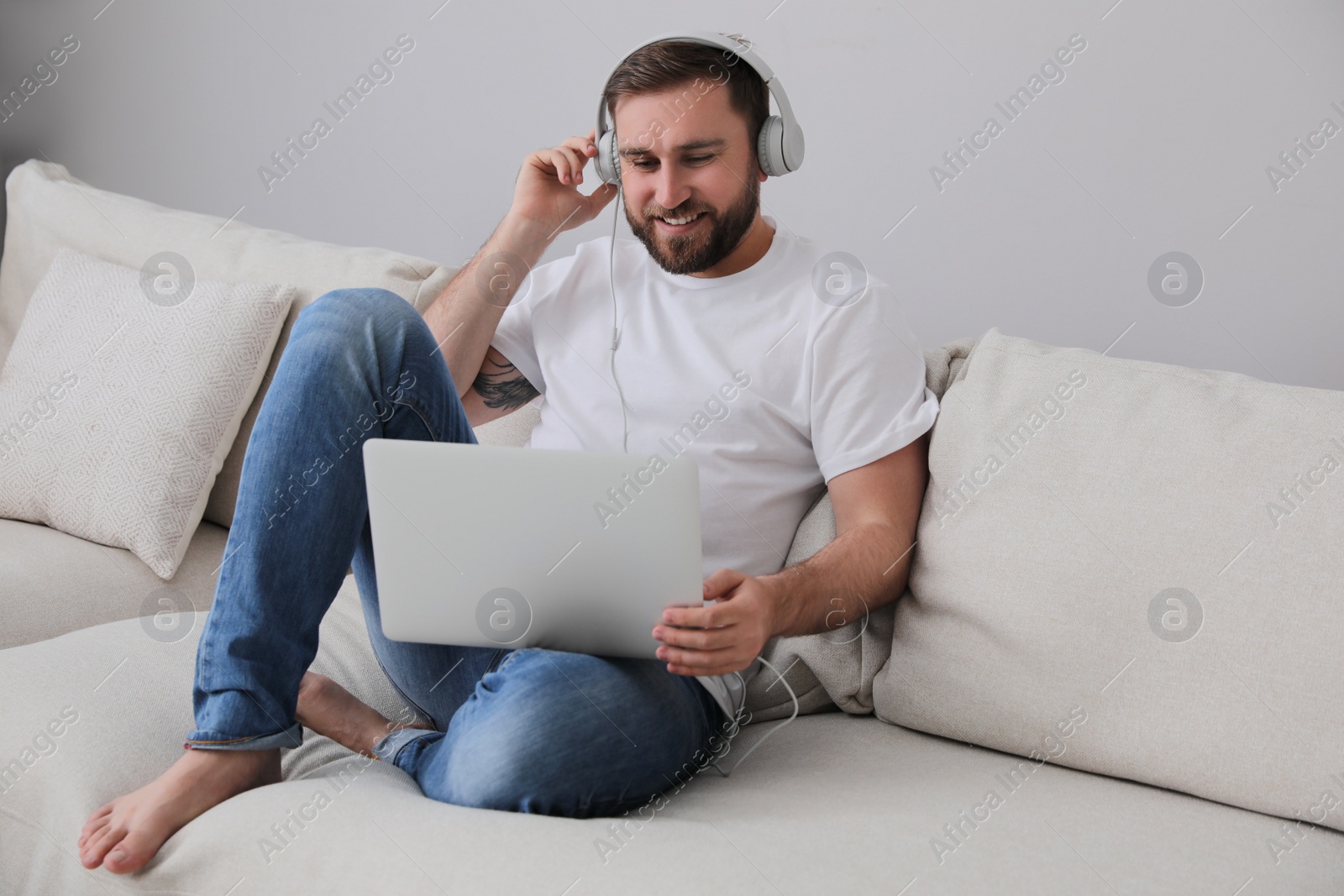 Photo of Man with laptop and headphones sitting on sofa at home