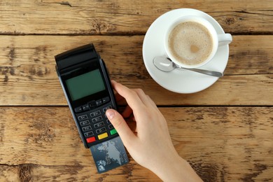 Woman with credit card using modern payment terminal at wooden table, top view