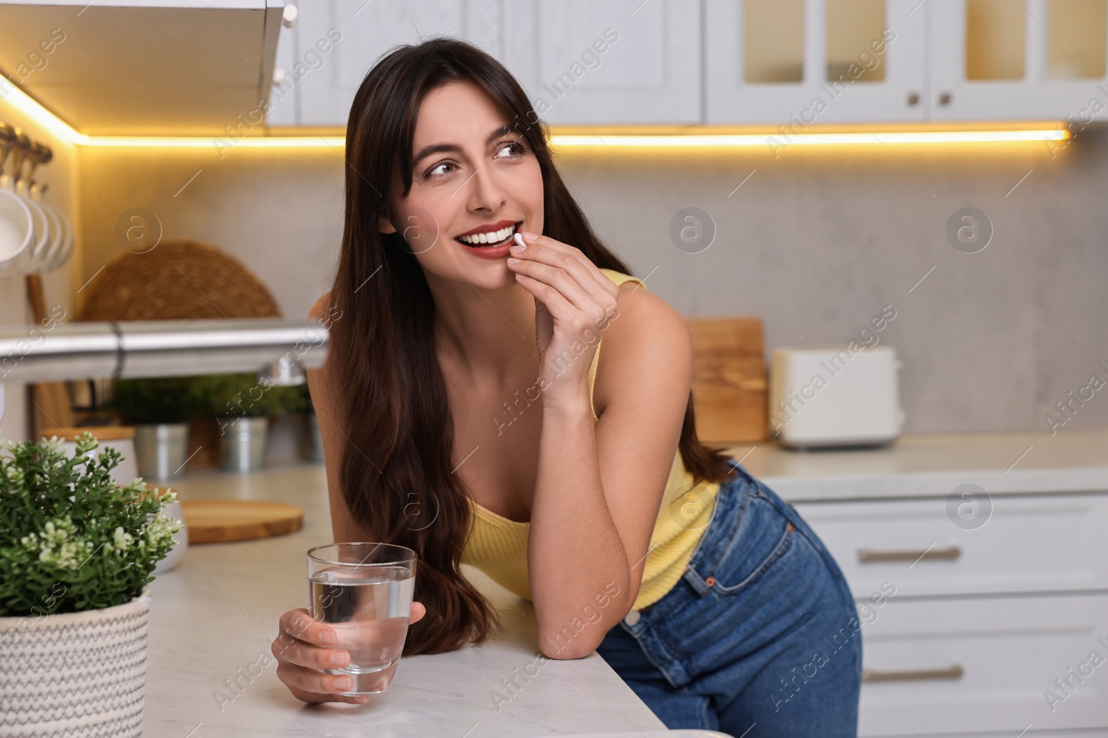 Photo of Beautiful woman taking vitamin pill at white table in kitchen