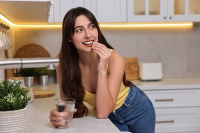 Photo of Beautiful woman taking vitamin pill at white table in kitchen