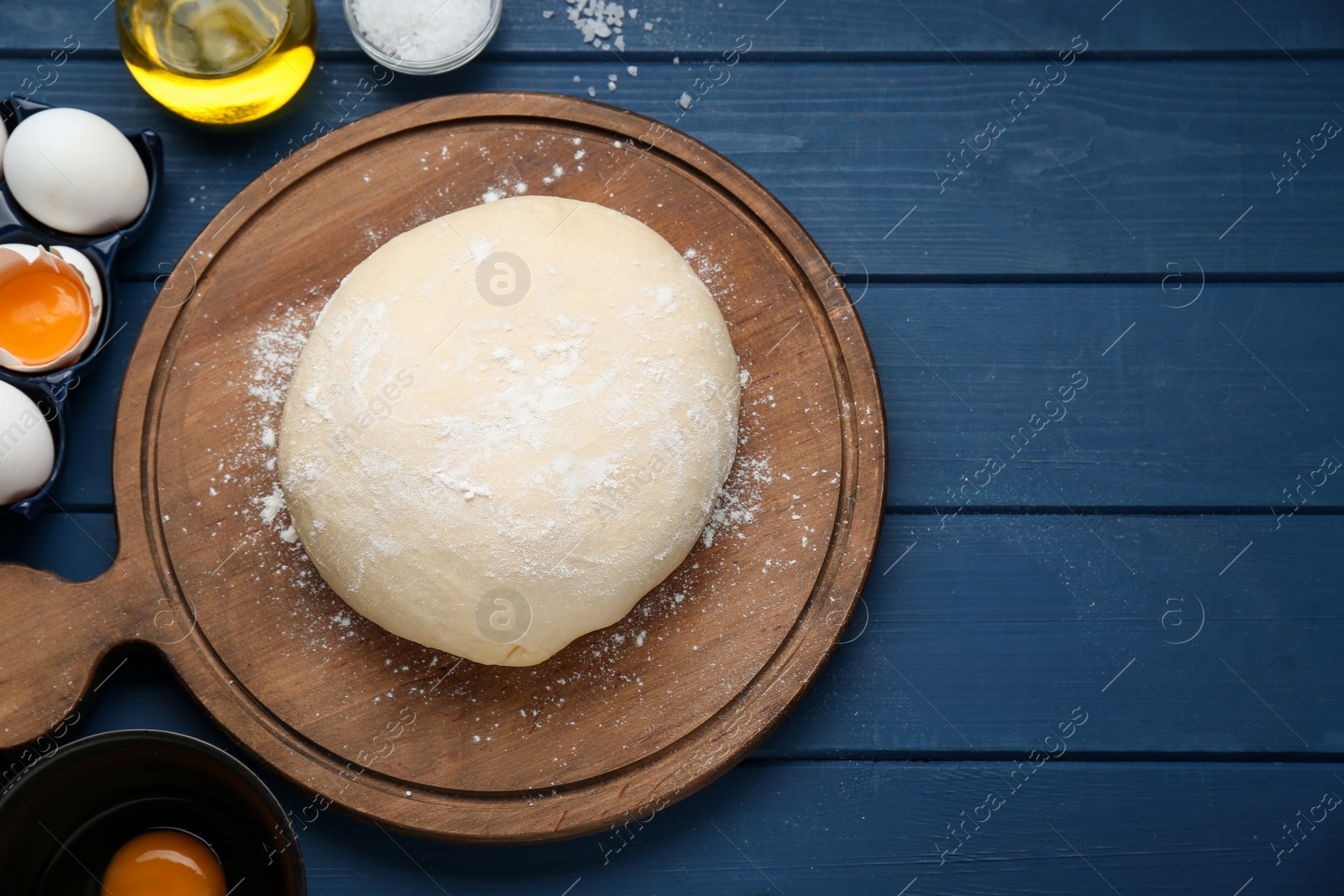 Photo of Fresh yeast dough and ingredients on blue wooden table, flat lay. Space for text