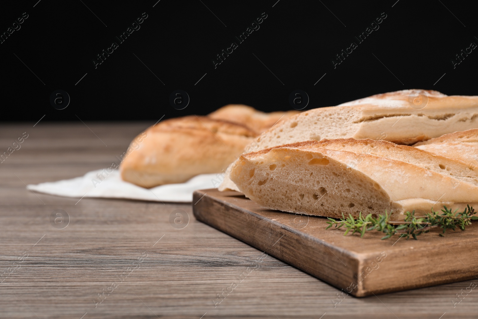 Photo of Cut tasty baguette with thyme on wooden table. Space for text