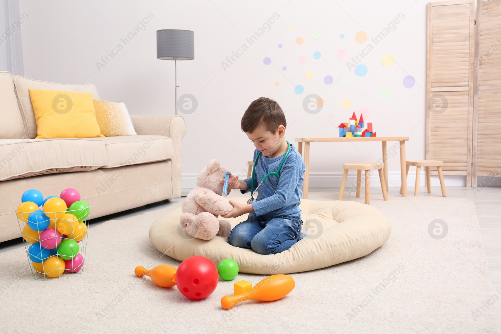 Photo of Cute child playing doctor with stuffed toy on floor in hospital