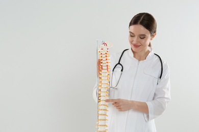 Photo of Female orthopedist with human spine model against light background. Space for text