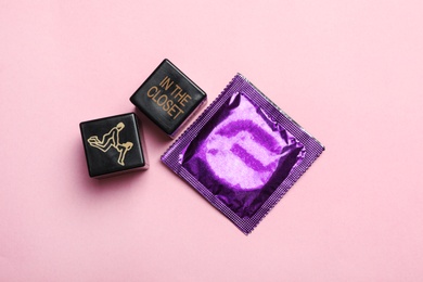 Photo of Sex dice and condom on pink background, top view