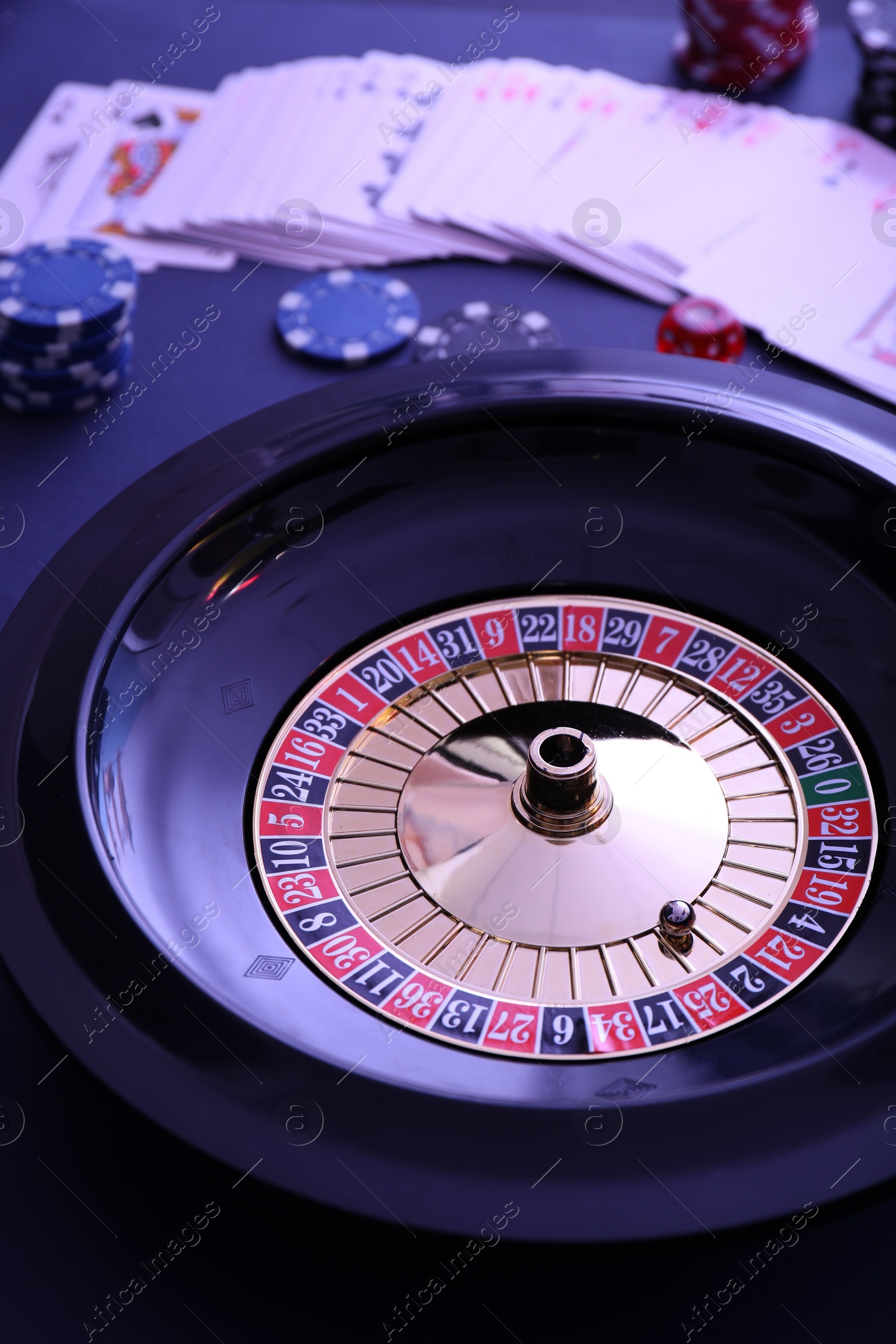 Photo of Roulette wheel, playing cards and chips on table, closeup. Casino game