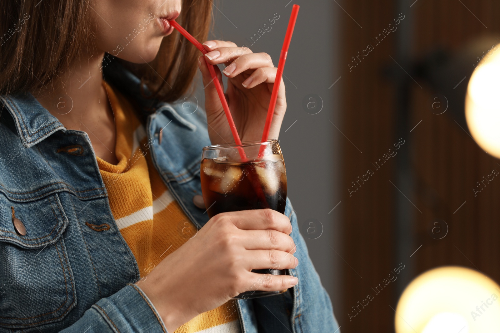 Photo of Woman drinking cola from glass against blurred background, closeup