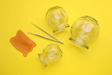 Photo of Glass cups, gua sha and tweezers on yellow background, flat lay. Cupping therapy