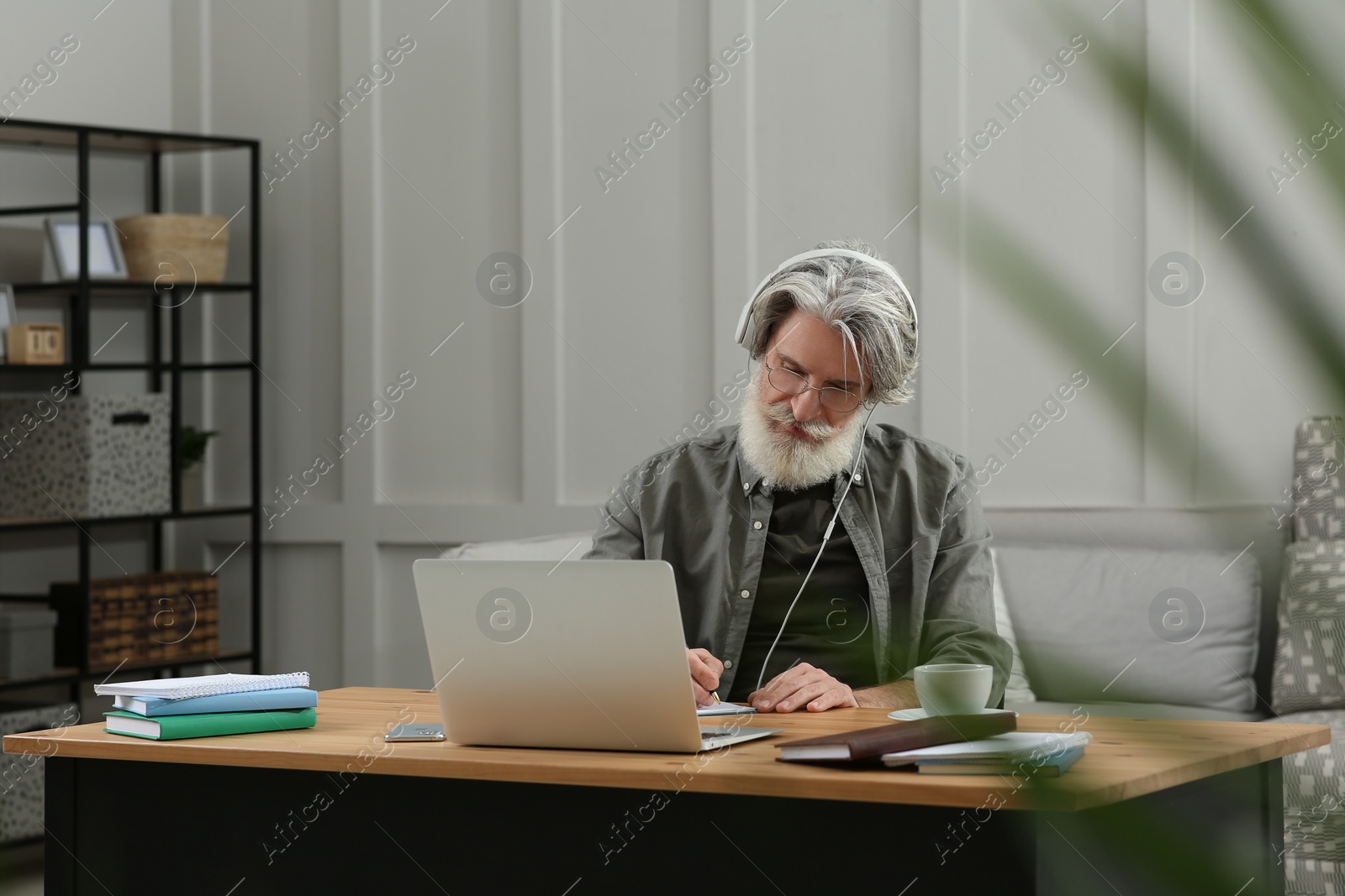 Photo of Middle aged man with laptop and headphones learning at table indoors