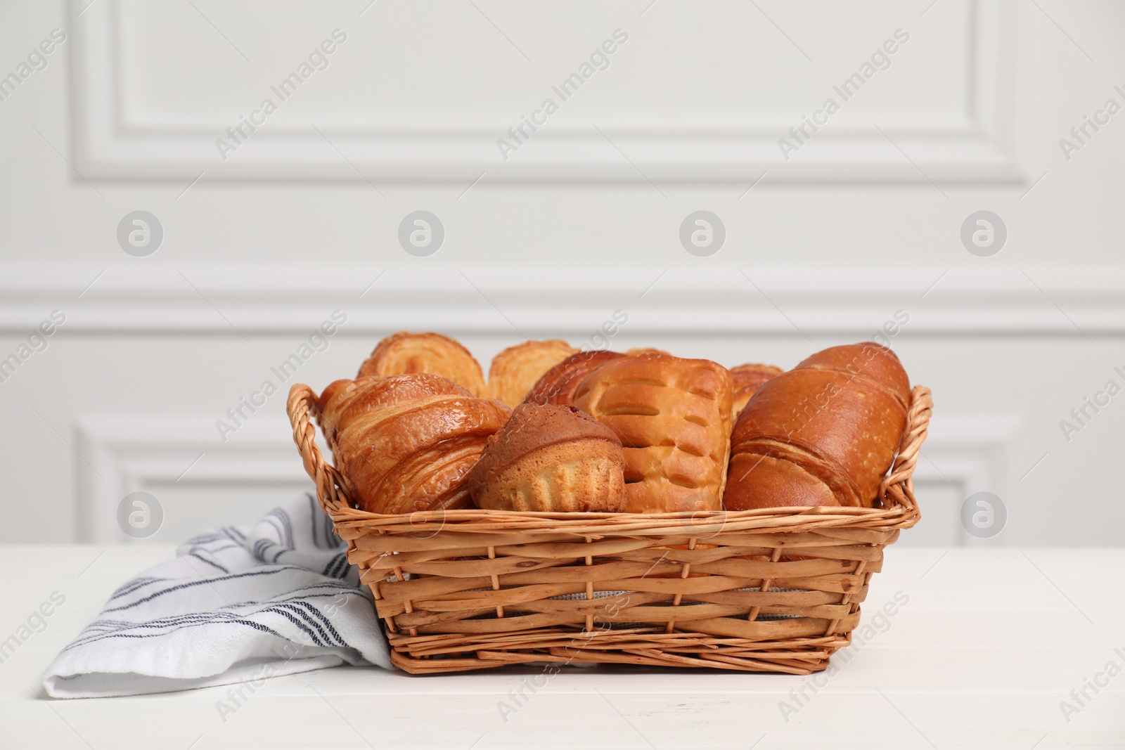 Photo of Wicker basket with different tasty freshly baked pastries on white wooden table, space for text