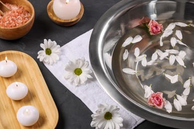 Photo of Bowl of water, flowers, burning candles and sea salt on dark table. Pedicure procedure