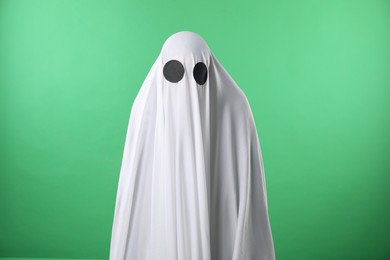 Photo of Creepy ghost. Person covered with white sheet on green background