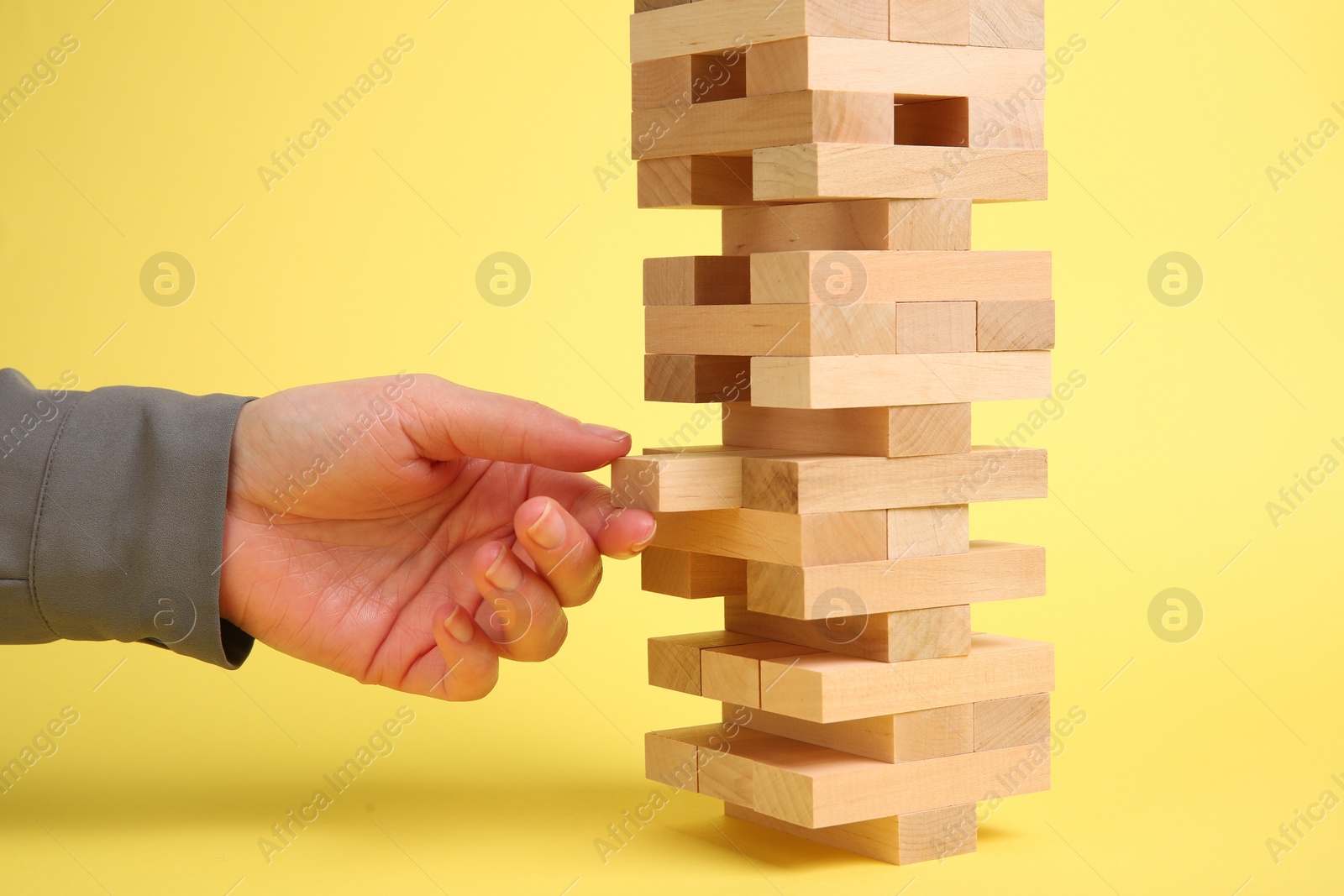 Photo of Woman playing Jenga tower on yellow background, closeup