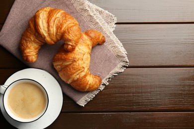 Photo of Delicious fresh croissants and cup of coffee on wooden table, flat lay. Space for text