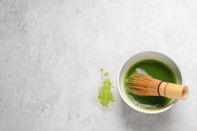 Bowl of fresh matcha tea with bamboo whisk and powder on light table, flat lay. Space for text