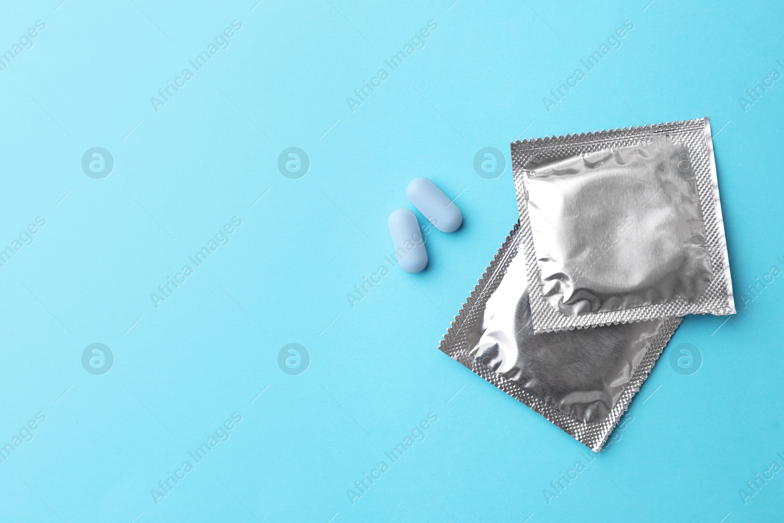 Photo of Pills and condoms on light blue background, flat lay with space for text. Potency problem