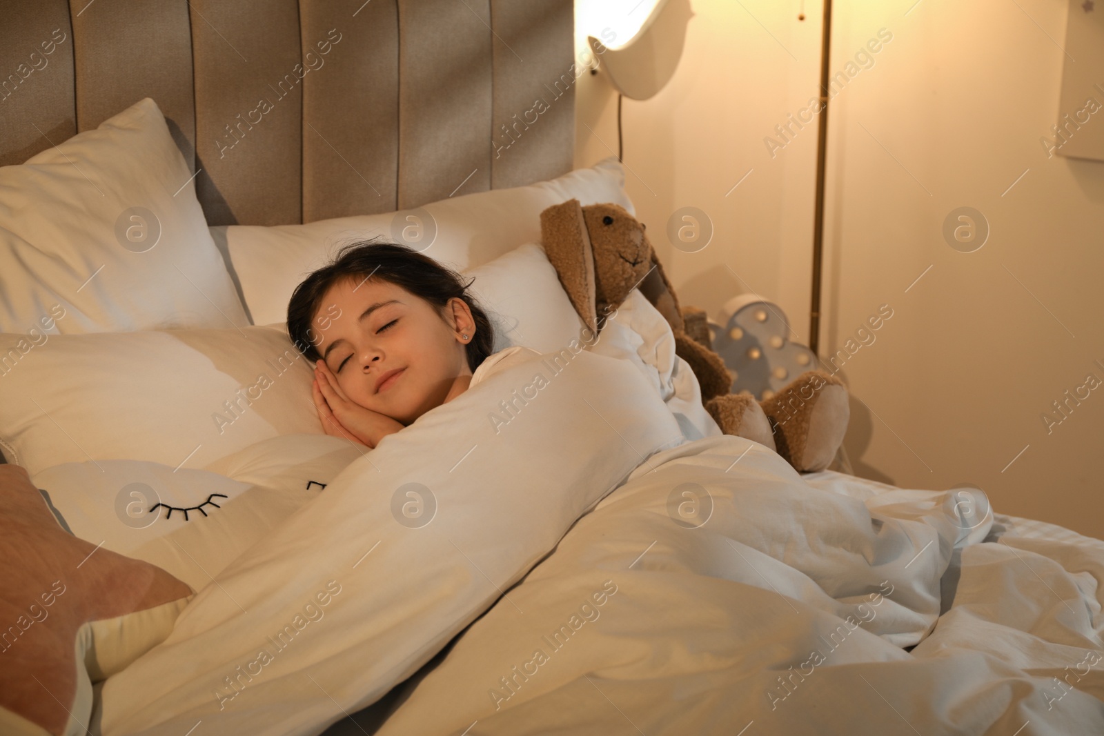 Photo of Little girl sleeping in bedroom lit by night lamp