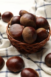 Sweet fresh edible chestnuts in wicker bowl on table, closeup