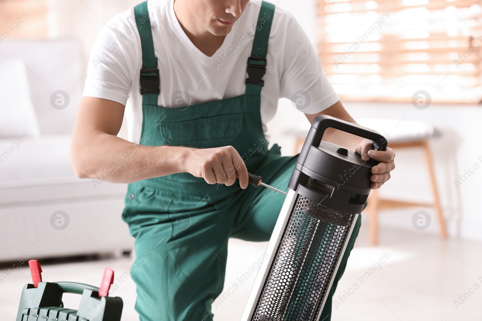 Photo of Professional technician repairing electric patio heater with screwdriver indoors, closeup