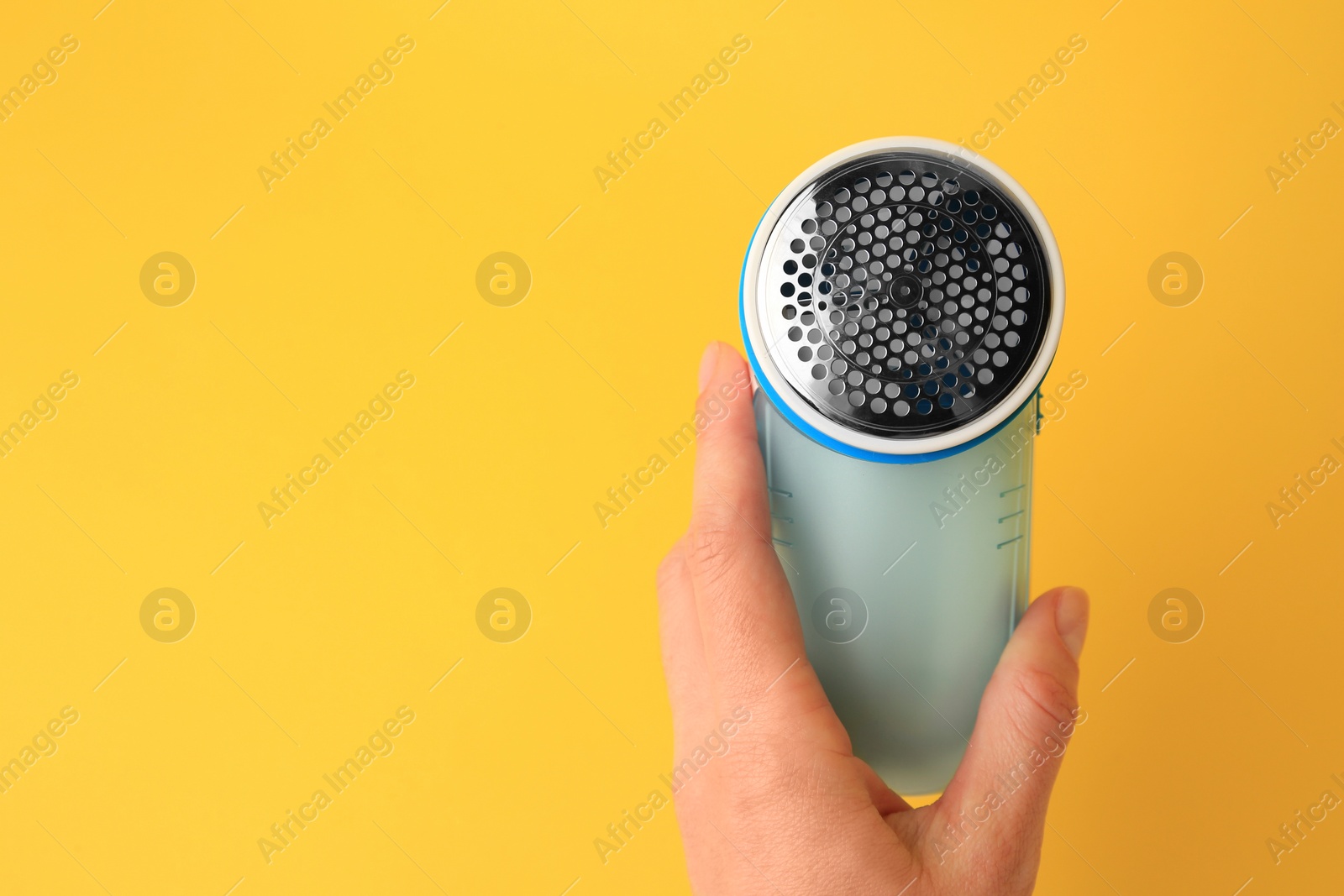 Photo of Woman holding modern fabric shaver on yellow background, closeup. Space for text