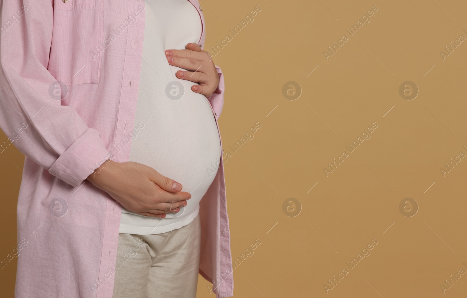 Photo of Pregnant woman on light brown background, closeup. Space for text