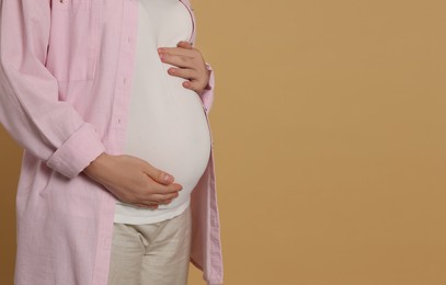 Pregnant woman on light brown background, closeup. Space for text