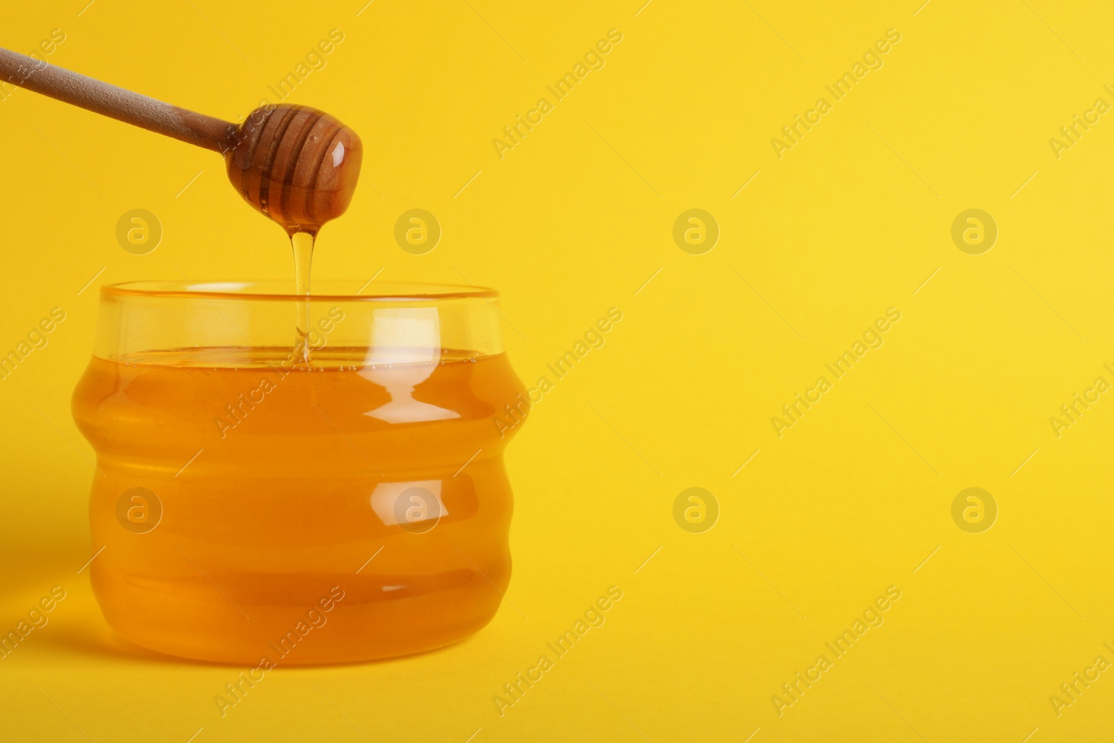 Photo of Jar with organic honey and dipper on yellow background. Space for text