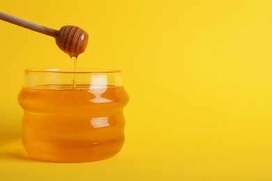 Jar with organic honey and dipper on yellow background. Space for text
