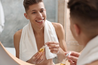 Photo of Handsome man with bottle of serum in bathroom