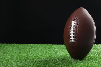 Photo of American football ball on green grass against black background, space for text