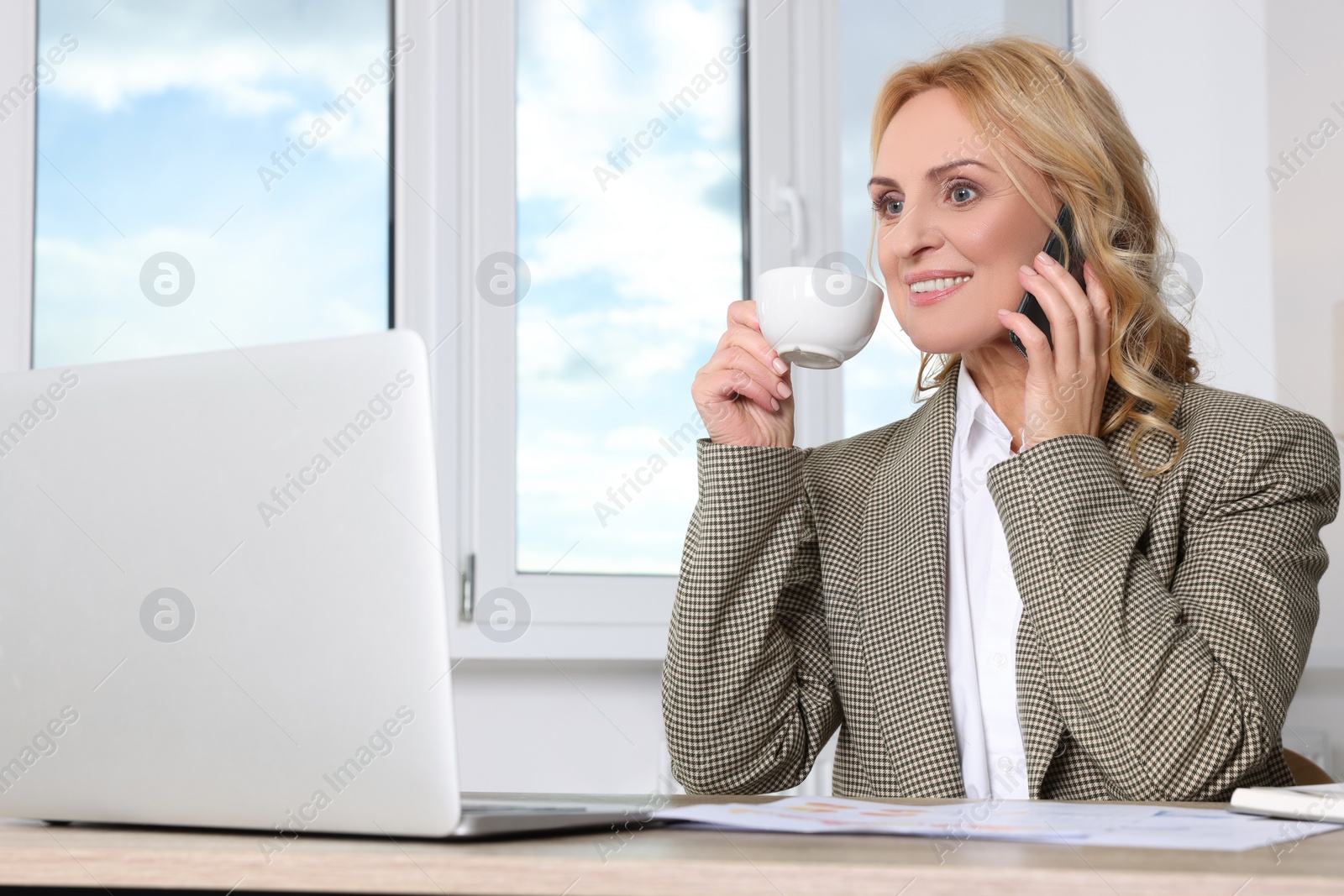 Photo of Lady boss talking on smartphone near laptop in office. Successful businesswoman