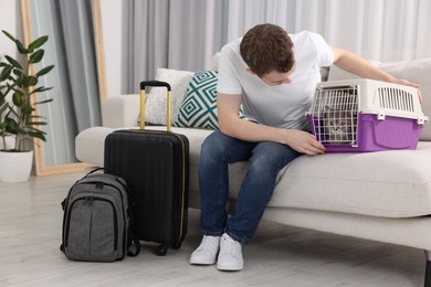 Photo of Travel with pet. Man closing carrier with cat on sofa at home