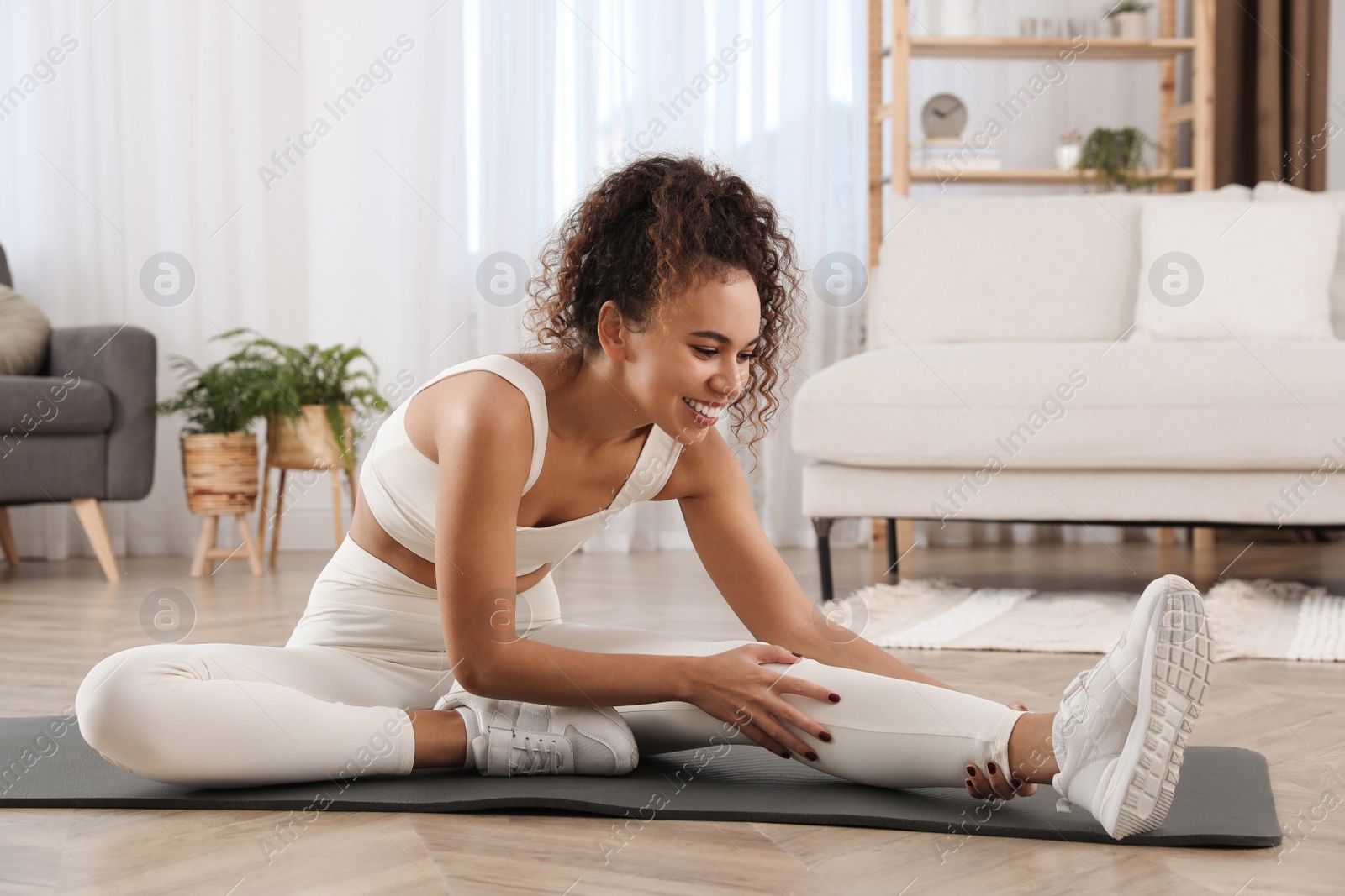 Photo of Beautiful African American woman stretching on yoga mat at home