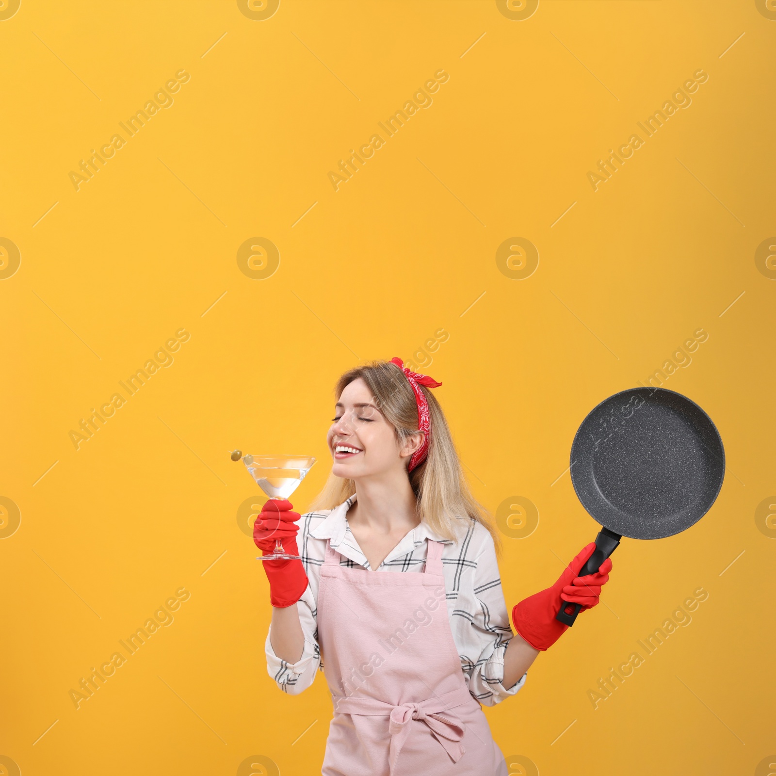 Photo of Young housewife with frying pan and glass of martini on yellow background