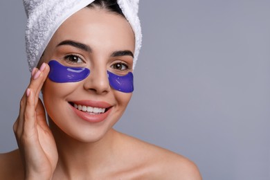 Photo of Beautiful young woman with under eye patches and hair wrapped in towel on grey background, space for text