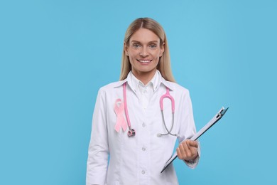 Doctor with pink ribbon, clipboard and stethoscope on light blue background. Breast cancer awareness