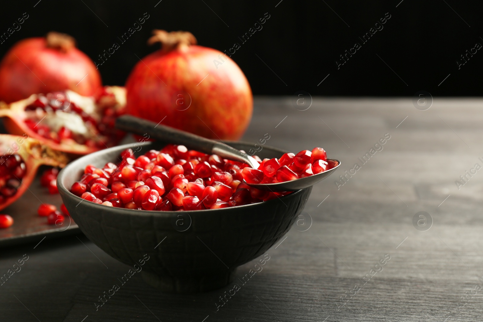 Photo of Tasty ripe pomegranates and grains on dark wooden table, closeup. Space for text