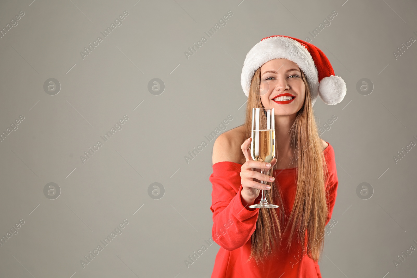 Photo of Young beautiful woman in Santa hat with glass of champagne on grey background. Christmas celebration
