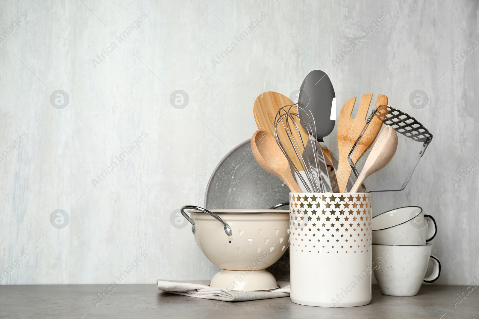 Photo of Different kitchen utensils on grey table against light background. Space for text