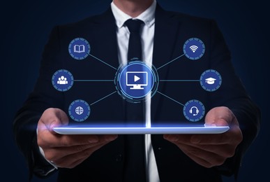 Image of Webinar. Man holding tablet on dark blue background, closeup. Virtual screen with icons over device