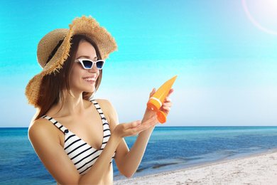 Young woman applying sun protection cream at beach, space for text
