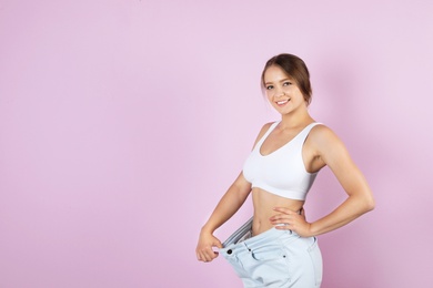 Young woman wearing oversize pants on color background. Healthy diet