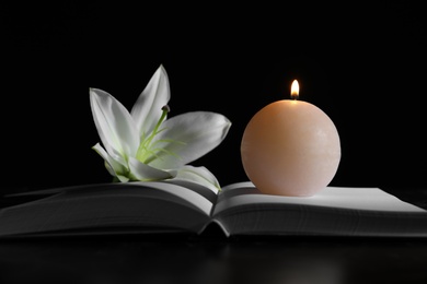 Photo of Burning candle, book and white lily on table in darkness. Funeral symbol