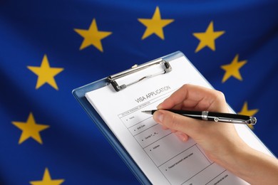 Photo of Woman filling visa application form against flag of European Union, closeup