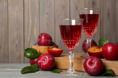 Photo of Delicious plum liquor and ripe fruits on grey wooden table, space for text. Homemade strong alcoholic beverage