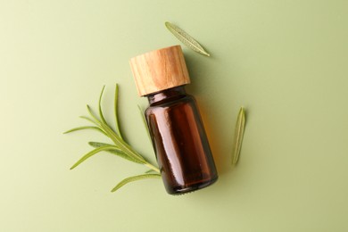 Aromatic essential oil in bottle and rosemary on green background, flat lay