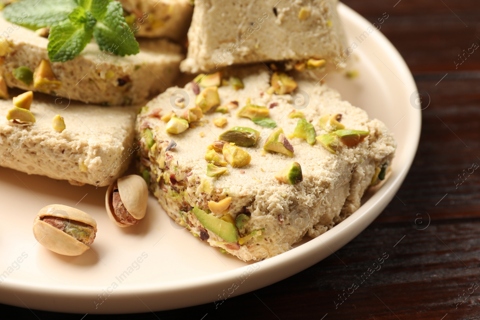 Photo of Pieces of tasty halva with pistachios and mint on table, closeup