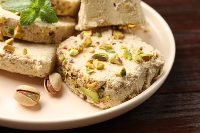 Photo of Pieces of tasty halva with pistachios and mint on table, closeup